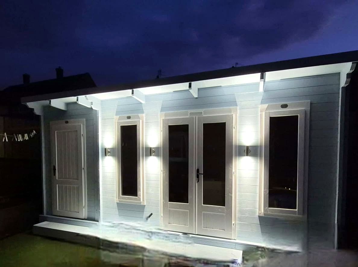 Wall lights and under-eave lighting on a garden room at night.
